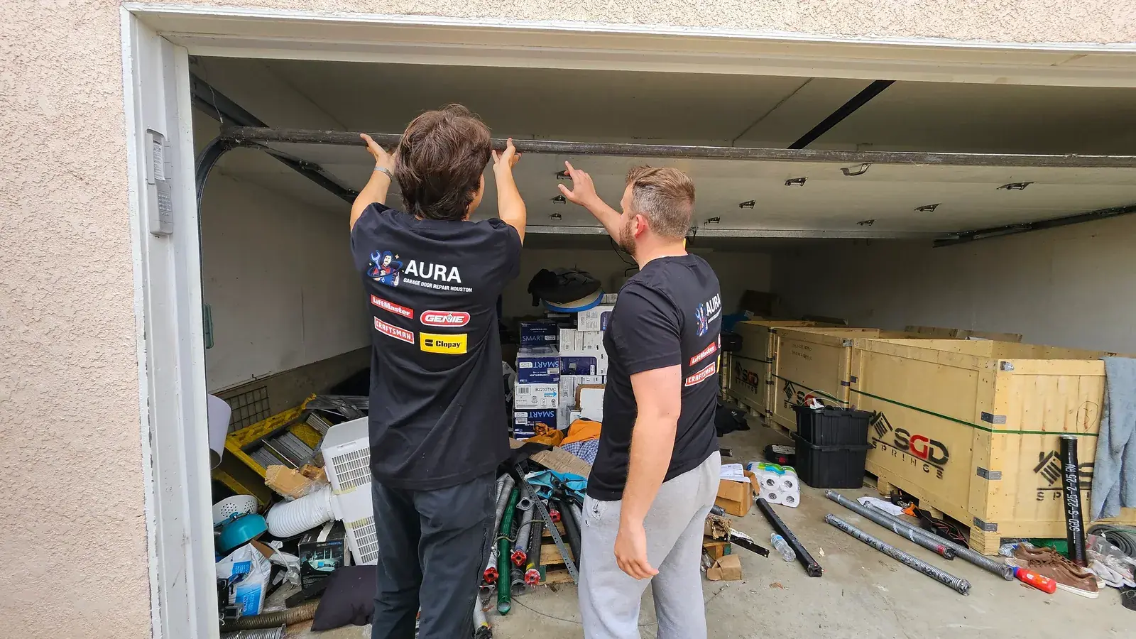 Two Aura technicians inspecting the overhead hardware of a garage door
