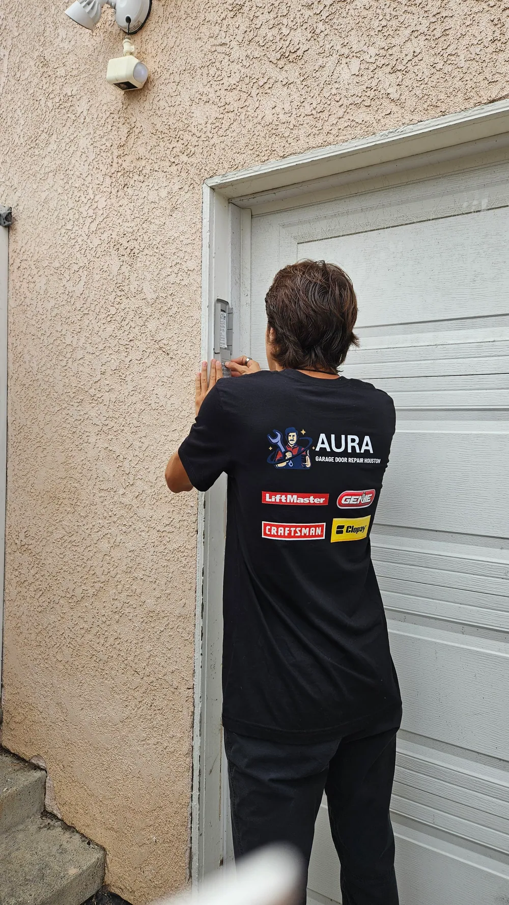 Aura technician in a branded shirt checking the side of a garage door