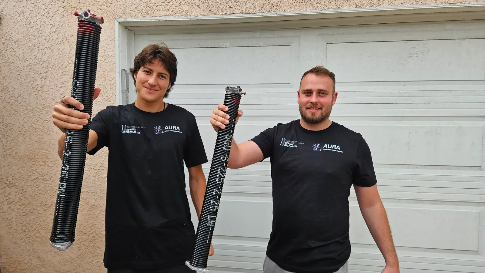 Two Aura technicians holding torsion springs at a customer garage